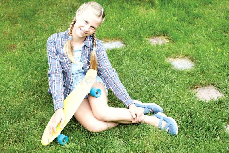 Appy Ð- och att skratta barnet som bär kalla modekläder som poserar med den färgrika skateboarden mot grönt gräs, stads- stil